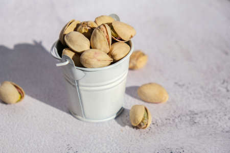 Pistachios in white bucket on concrete background. Healthy and dietary nutrition. Concept of nuts. Vegan protein omega vitamin food. Roasted salty pistachio. Harvestの写真素材