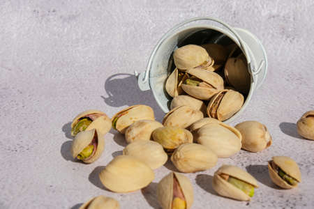 Pistachios in white bucket on concrete background. Healthy and dietary nutrition. Concept of nuts. Vegan protein omega vitamin food. Roasted salty pistachio. Harvestの写真素材