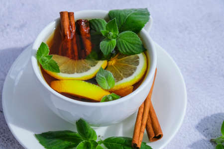 Black and green tea with lemon, cinnamon sticks and mint leaves. Hot drink. Healthy melissa tea natural organic aromatic drink in cup. Summer, Autumn winter warming drink. Stay healthy herbal teaの写真素材