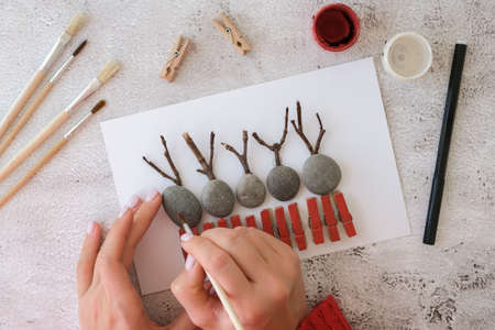 Diy Merry Christmas deer on greeting card postcard made of pebbles, sea stones, clothespins and branches on white background. Natural Eco style diy. Gift idea. Step by step. Top view. Process kid children craft. Do it yourselfの写真素材