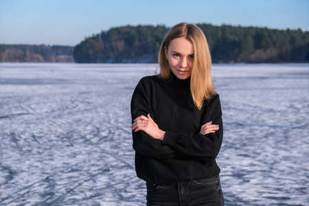 Young female smiling and looking at a camera in a snow landscape. Happy hipster girl with hip hop warm winter clothes. Staying on frozen river, lake.の写真素材