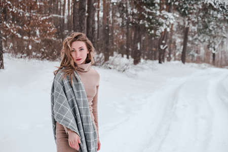 Happy woman on the winter forest background. Young pretty girl in the woods outdoors. Portrait of a cheerful beautiful woman. Winter fashion. Dress with scarfの写真素材