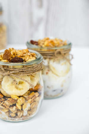 Healthy breakfast. Oatmeal Granola with greek yogurt and nuts banana muesli in jars on light background. Vegan, vegetarian and weight loss diet concept. Detox menu. Healthy eating foodの写真素材