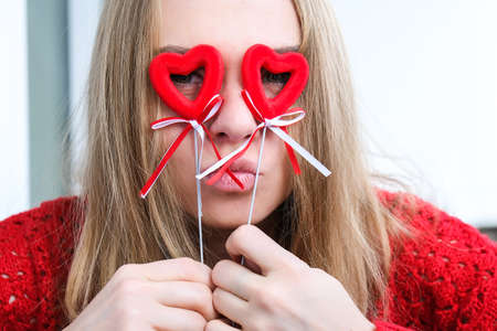 Young blonde girl in red sweater holding red hearts showing emotions. Taking selfie. Video chat....