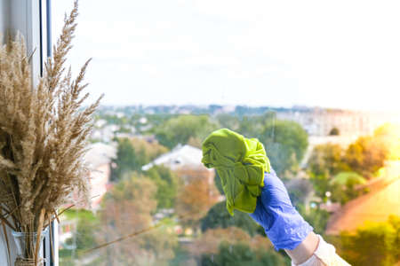 Employee hand in rubber protective glove with micro fiber cloth wiping window from dust. General spring cleaning. Housework and housekeeping concept. Wiper with a dirty window from the outsideの写真素材