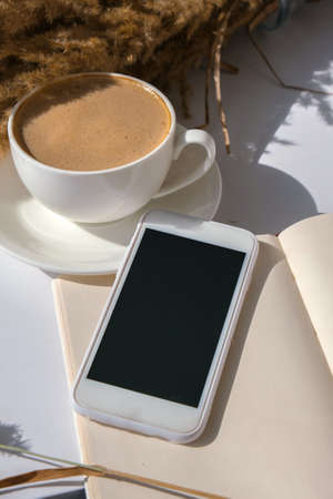 Pampas grass and white cup with coffee. Mobile phone with black screen. Checking social media Drinking Cappuccino in the breakfast morning at home. Flat lay. Wallpaper. Aestheticsの写真素材