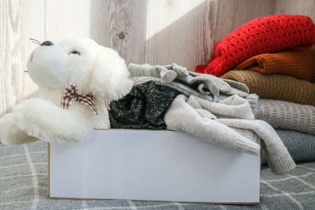 Donation box with old used toys and clothes indoors. Happy Charity. Box with clothes in it. close-up. Clothing donation. Winter clothes in a cardboard box. Seasonal clothingの写真素材