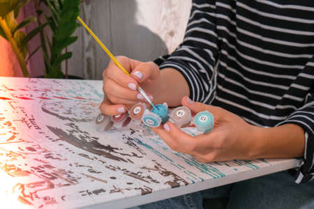 Painting on canvas by numbers and numbered jars of paint. Woman draws with a brush painting by numbers on canvas. Creative hobby. Painting for beginners. Leisure activity for stay home lockdown, anti-stress idea. Meditation, relax conceptの写真素材