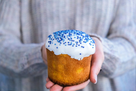 The cook Hands hold Easter cake with white topping and blue sprinkles. Woman holding traditional Russian Easter cake. Homemade pie for spring holiday celebrationの写真素材
