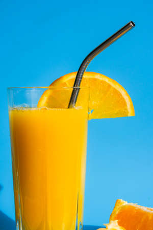 Glass of fresh squeezing Orange juice with eco metal drinking straw sliced fruits on blue background. Fruit juice, fresh cold drink. Refreshment in summer. Clean eating, weight loss, healthy dieting foodの写真素材
