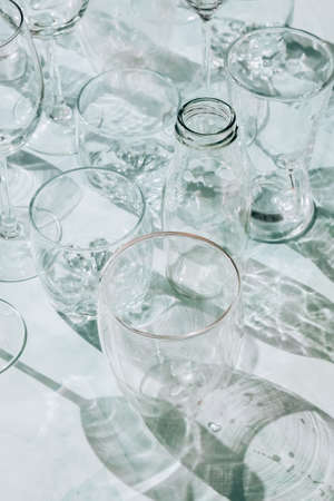 Beautiful different glasses stand on white background in sunlight and create shadows. Hard light, long shadows. Creative concept of drinks, alcohol cocktails. Glassware concept. Geometric shapesの写真素材