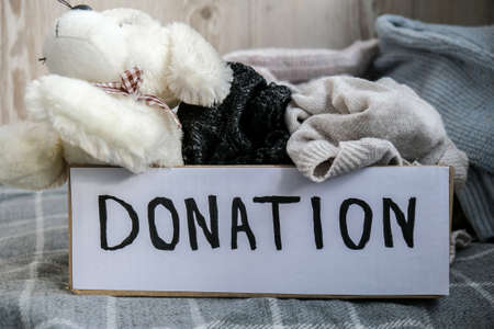 Donation box with old used toys and clothes indoors. Happy Charity. Box with clothes in it. close-up. Clothing donation. Winter clothes in a cardboard box. Seasonal clothingの写真素材