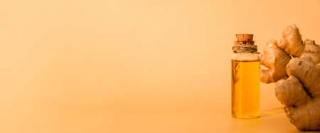 Glass bottle of essential ginger oil, ginger root on beige background. Healthy food eating concept. Zingiber officinale Essential oil. Earth tones Natural cosmetics ingredients for skincare, body and hair care. Banner Copy spaceの写真素材