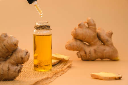 Glass bottle of essential ginger oil, ginger root on beige background. Healthy alternative living. Zingiber officinale Natural cosmetics ingredients for skincare, body and hair careの写真素材