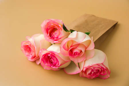 Delicate pink roses in craft paper bag on beige background. Minimal trendy composition. Abstract art idea. Romantic pastel pink rose flowers. Modern aesthetic. Neutral earth tones. Greeting card background Copy space Bannerの写真素材