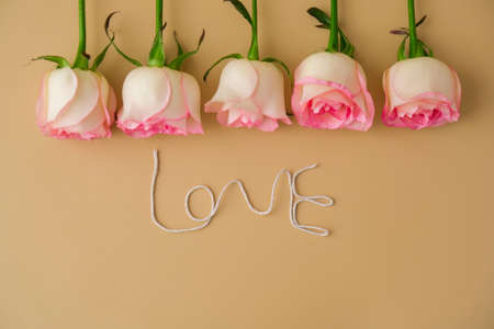 Delicate pink roses on beige background. Word LOVE made of rope. Minimal trendy composition. Romantic pastel pink rose flowers. Neutral earth tones. Greeting card for Valentines day Modern stylishの写真素材
