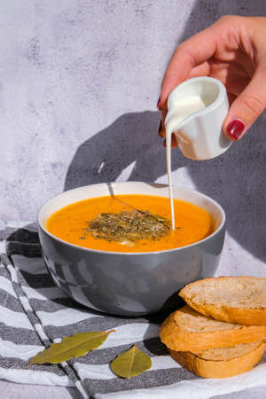 Woman adding cream to Homemade carrot ginger curcuma soup. Female hand pouring milk into Seasonal Pumpkin traditional soup with creamy silky texture. Healthy vegan clean eating.の写真素材