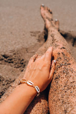 Womans hands with shell jewelry in sand. Sand in hands on the beach. Travel and vacation concept....