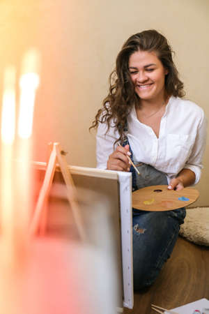 Creative painter in working process. Artist workplace, hobby, craft tools. Artist female canvas painting. Professional young woman painter draws in the workshop. Leisure activity. Art at homeの写真素材