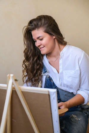 Creative painter in working process. Artist workplace, hobby, craft tools. Artist female canvas painting. Professional young woman painter draws in the workshop. Leisure activity. Art at homeの写真素材