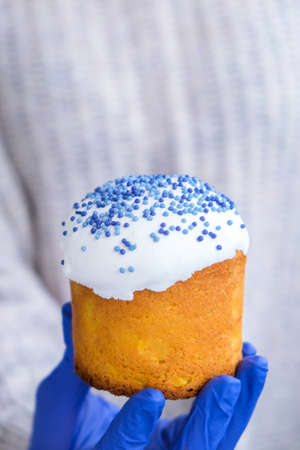 The cook Hands in blue gloves hold Easter cake with white topping and blue sprinkles. Woman holding...