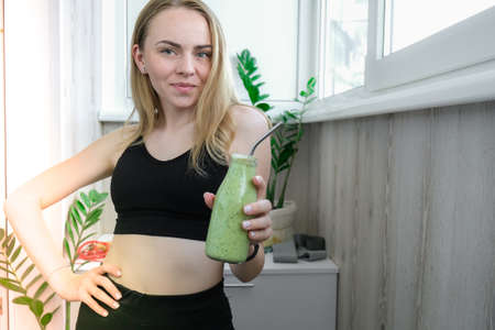 Young millenial blond woman drinking vegan smoothie drink detox. Woman doing yoga exercises at home. Clean eating, weight loss, healthy dieting food concept. Stay healthyの写真素材