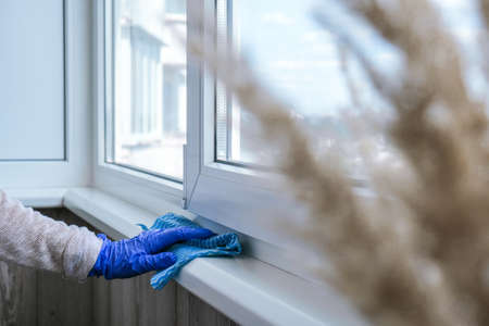 Cleaning the windowsill wiping dust by blue microfiber cloth for cleaning on the glass window rail Blue Gloves Cleaning Using Sprayed Liquid. Housework and housekeeping concept. Springの写真素材