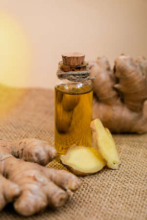 Glass bottle of essential ginger oil, ginger root on beige background. Healthy food eating concept. Zingiber officinale Essential oil. Natural cosmetics ingredients for skincare, body and hair careの写真素材