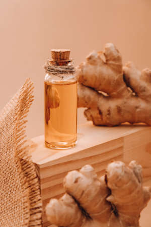 Glass bottle of essential ginger oil, ginger root on beige background. Healthy alternative living....