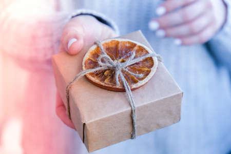 Woman giving Box with New Year's gifts, wrapped in craft paper and decorated with dry orange slices. Holidays and Gifts concept. Handmade Eco friendly alternative green Christmas presents zero waste Sustainable lifestyleの写真素材