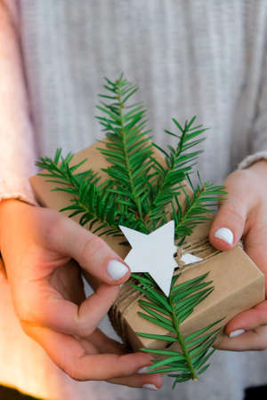 Woman giving Box with New Years gifts, wrapped in craft paper and decorated with fir branch. Holidays and Gifts concept. Handmade Eco friendly alternative green Christmas presents zero wasteの写真素材