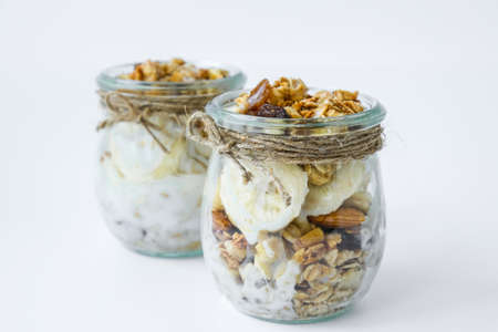 Healthy breakfast. Oatmeal Granola with greek yogurt and nuts banana muesli in jars on light...