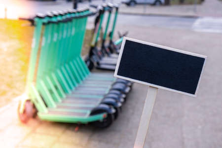 Empty mockup template Blackboard label against electric scooters parked on city street. Self-service street transport rental service. Rent urban vehicle with smartphone application. Zero emission green eco energy. E-scooters for hire alternative eco friendly vehicleの写真素材