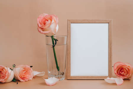 Mockup Wooden frame with Empty white paper blank and delicate pink roses on beige background. Minimal trendy composition. Romantic pastel pink rose flowers. Neutral earth tones. Copy space Greeting card holiday Valentines Mothers Womens dayの写真素材