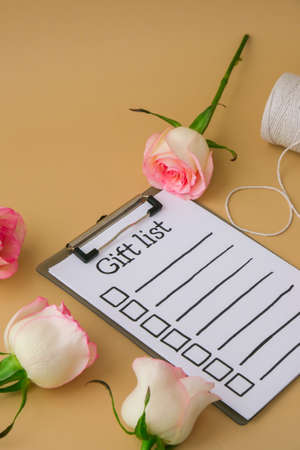 GIFT LIST text on paper note. Delicate pink roses with spool of white cotton rope on beige background. Minimal trendy composition. Romantic pastel pink rose flowers. Neutral earth tones. Preparation for Valentines day Modern stylishの写真素材