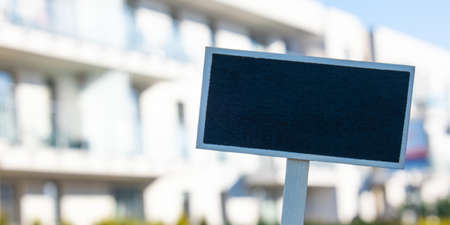 Blank Black billboard against new apartment building Empty mockup template Blackboard label Home for rent. Apartments for sale. Sign in front of new home. Advertisementの写真素材
