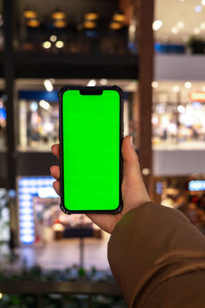Chrome key. Close up of woman hand holds smart phone vertical with green screen at shopping mall store. shopping center. department stores. shopping online. Gadgets Advertisement template mockupの写真素材