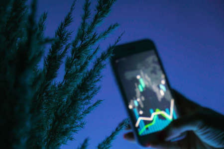 Defocused Woman holding mobile phone, block chain with graph of stock market background, cryptocurrencies or bitcoin concept. night light. Futuristic stock exchange with general info shown on screenの写真素材