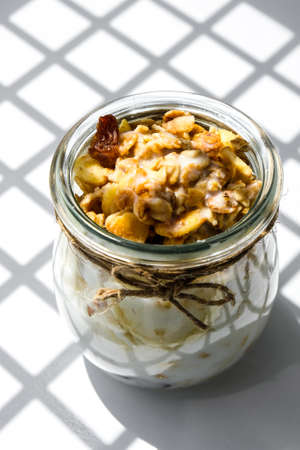 Healthy breakfast. Oatmeal Granola with greek yogurt and nuts banana muesli in jars on light background. Trendy shadows Vegan, vegetarian and weight loss diet concept. Detox menu. Healthy foodの写真素材