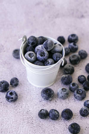 Frozen Blueberries in small Bucket on concrete background. Healthy organic seasonal fruit...