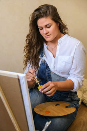 Creative painter in working process. Artist workplace, hobby, craft tools. Artist female canvas painting. Professional young woman painter draws in the workshopの写真素材