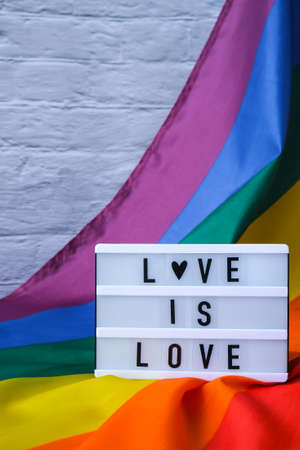 Rainbow flag with lightbox and text LOVE IS LOVE. Rainbow lgbtq flag made from silk material. Symbol of LGBTQ pride month. Equal rights. Peace and freedom. Support LGBTQ communityの写真素材