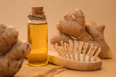 Glass bottle of essential ginger oil, ginger root on beige background. Healthy alternative living....