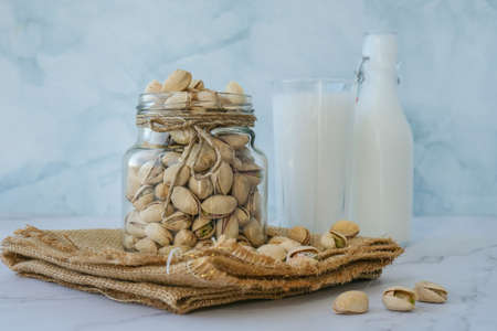 Glass of healthy pistachio milk stands on concrete background. Diet milk, vegetarian food. Gluten...