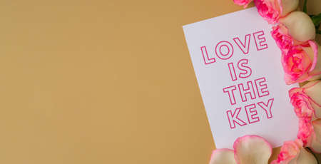 LOVE IS THE KEY text on greeting card paper note. Delicate pink roses on beige background. Minimal trendy composition. Romantic pastel pink rose flowers. Neutral earth tones. Preparation for Valentines day Modern stylish Copy space Bannerの写真素材