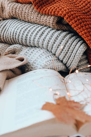 Book on first plan Thanksgiving and Hello Fall, celebrating autumn holidays at cozy home on the windowsill Hygge atmosphere Autumn leaves, spices and candle on cozy knitted sweater in warm yellow lights. selective focusの写真素材