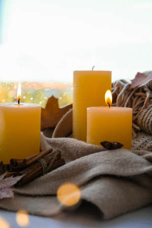 Hello Fall, celebrating autumn holidays at cozy home on the windowsill Hygge atmosphere Thanksgiving leaves, spices and candle on cozy knitted sweater in warm yellow lights. Selective focus Raining Outside the windowの写真素材