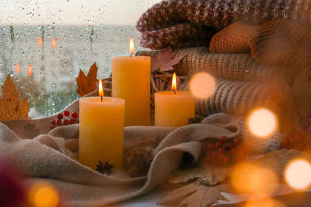 Hello Fall, celebrating autumn holidays at cozy home on the windowsill Hygge atmosphere Thanksgiving leaves, spices and candle on cozy knitted sweater in warm yellow lights. Selective focus Raining Outside the windowの写真素材