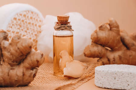 Glass bottle of essential ginger oil, ginger root on beige background. Healthy alternative living....