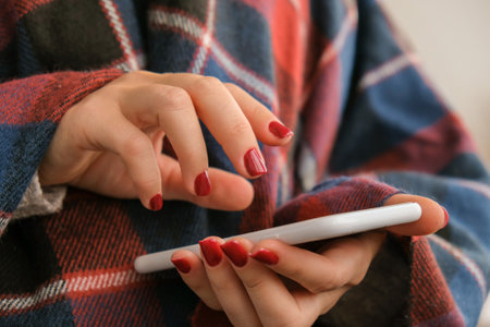 Stylish red female nails holding mobile phone. smartphone technology. social media. Modern Beautiful manicure. Autumn winter nail design concept of beauty treatment. gel nails. skincare. wellness. trendy colors.の写真素材